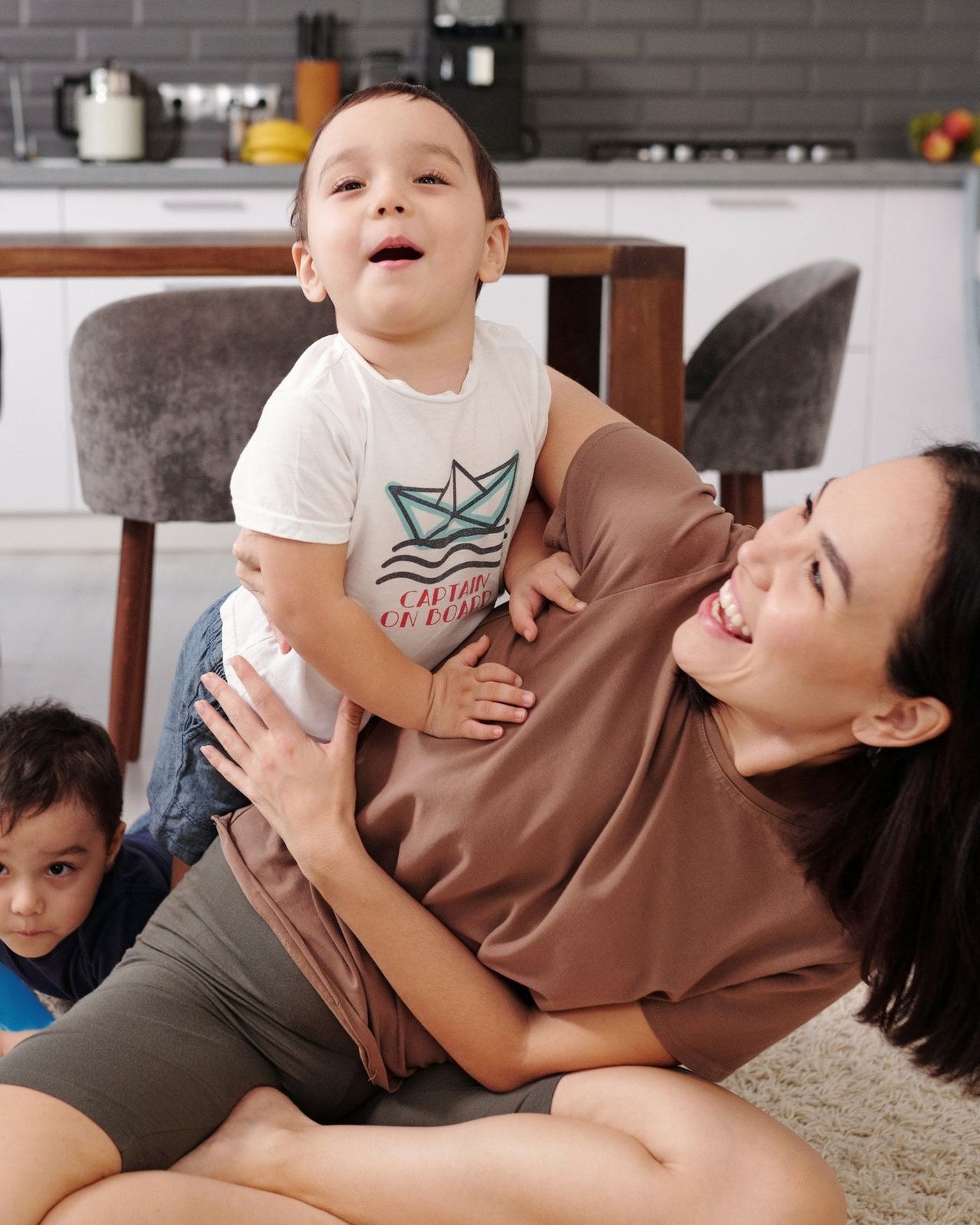 Madre riéndose mientras levanta a su hijo en la cocina